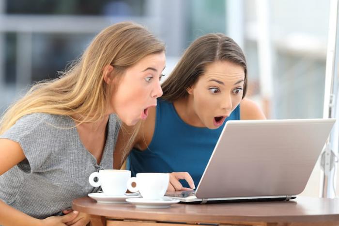 zwei junge Frauen mit langen Haaren, die überrascht auf einen Laptop schauen
