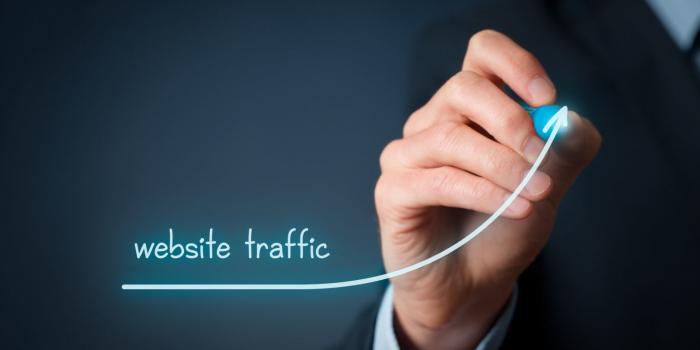 Bild einer Hand die die Worte website traffic und einen steigenden Pfeil auf die Linse schreibt