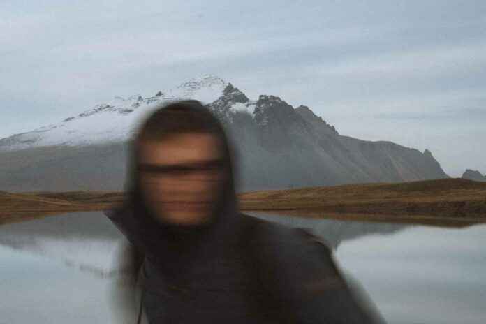 Bild einer Person, die vor einem See und Berg sehr verschwommen aufgenommen wurde