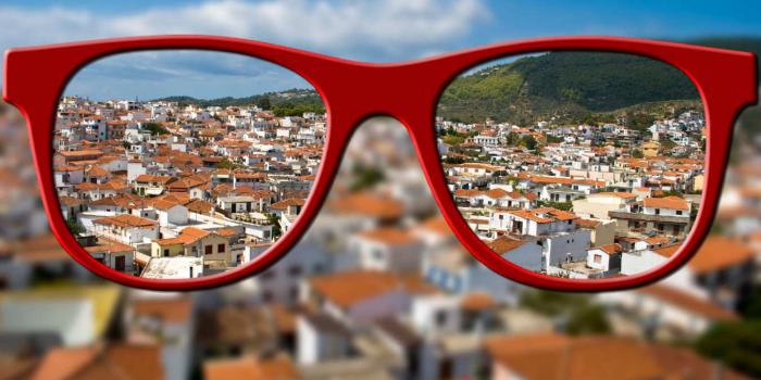 Verschwommenes Bild einer Stadt, das durch den Blick einer roten Brille scharf wird
