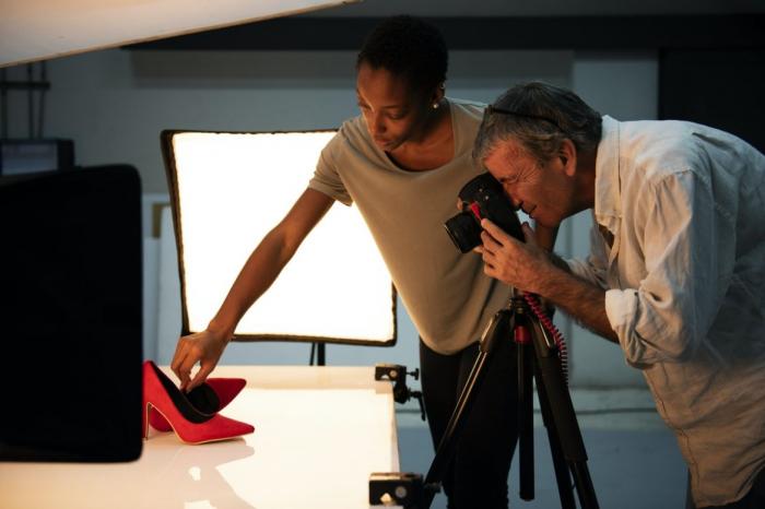 eine Frau die Schuhe platziert während ein Fotograf Produktfotos der Schuhe schießt