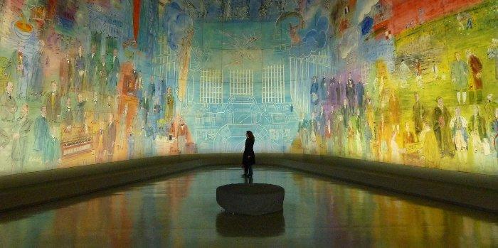 Eine Person, die in der Mitte eines Museums steht und Kunstwerke an digitalen Leinwänden bewundert