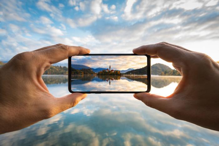 zwei Hände die mit einem Smartphone ein Foto von einer Inseln in einem See machen