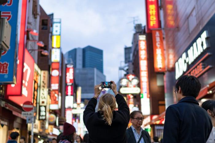 ein blonde Frau macht mit Ihrem Smartphone ein Foto von einer Straße in Tokio