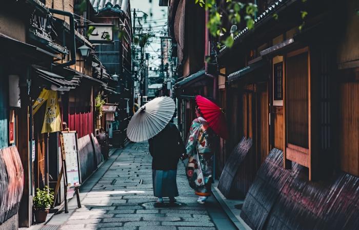 eine japanische Gasse, in der zwei Frauen in traditioneller japanischer Kleidung und mit Schirmen herunterlaufen