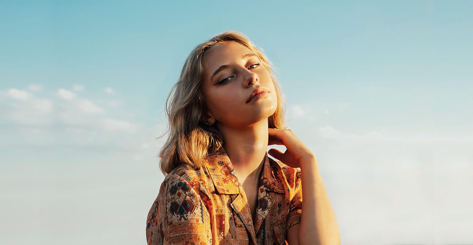 Bild einer jungen Frau mit blondem welligen Haar im Sonnenschein vor blauem Himmel